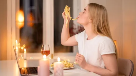 donna mangia un piatto di pasta davanti al pc